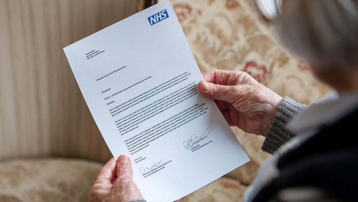 An elderly woman reading a letter from her NHS health care team conveying terminal diagnosis news